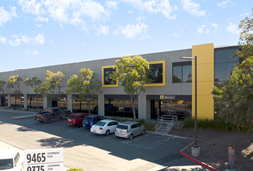 A row of office spaces with a paved parking lot in front of it.